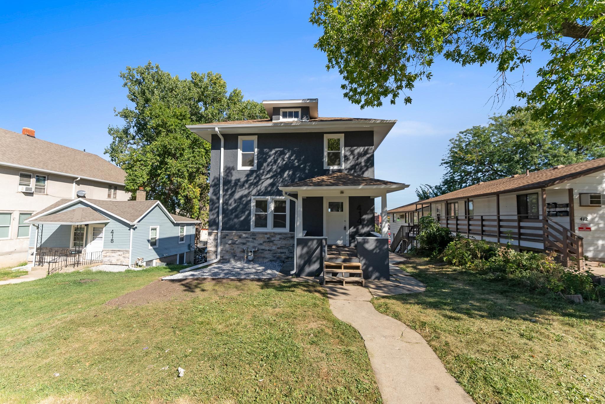 A quaint Cape Cod-style home with beige siding and white window frames, nestled among mature trees in a lush green lawn, located at 2201 S Euclid Ave, Sioux Falls, SD.