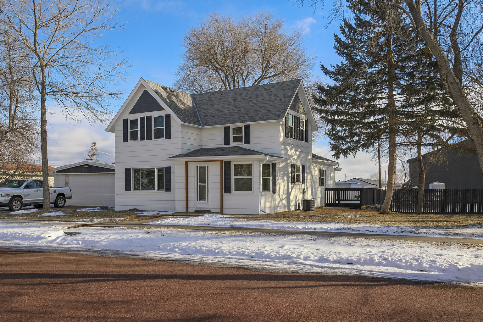 A quaint Cape Cod-style home with beige siding and white window frames, nestled among mature trees in a lush green lawn, located at 2201 S Euclid Ave, Sioux Falls, SD.